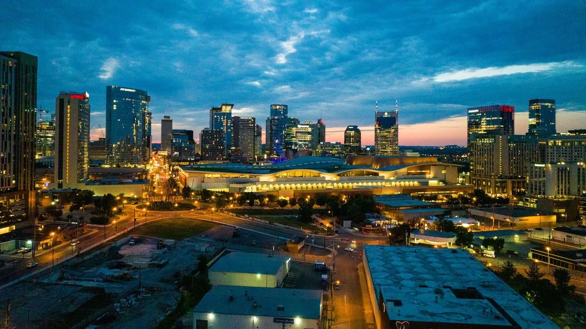 A striking view of the city skyline with illuminated buildings under a dusky sky, evoking the vibrant nightlife and urban energy of Nashville. The expansive cityscape suggests endless possibilities for dining, music, and entertainment.