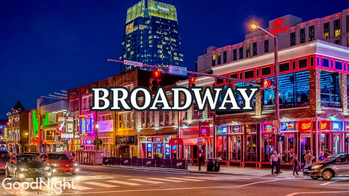 A vibrant city street scene with neon signs, busy sidewalks, tall buildings, and traffic lights—capturing the classic Nashville nightlife experience of dining, live music, and entertainment. The atmosphere is energetic and unmistakably urban.