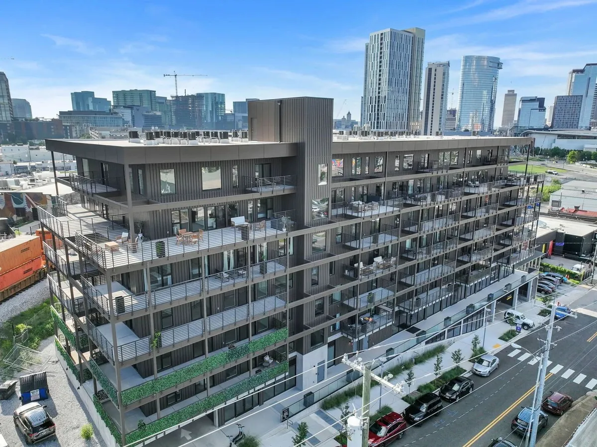 This exterior image captures the modern architecture of the condo building, highlighting its expansive balconies and the inviting landscaped rooftop and communal spaces. The visible balconies connect directly to the section's mention of private outdoor areas ideal for coffee or cocktails, while the rooftop area hints at amenities like the lounge and firepits.