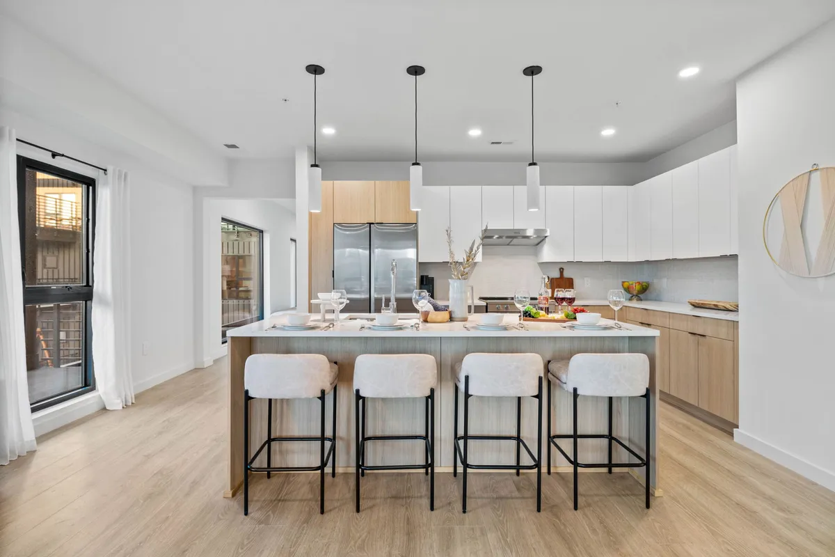 A close-up perspective on the modern kitchen, highlighting the kitchen island with bar stools, stainless steel appliances, a well-set dining table, and stylish pendant lights. The space is ready for hosting, cooking, and casual meals.