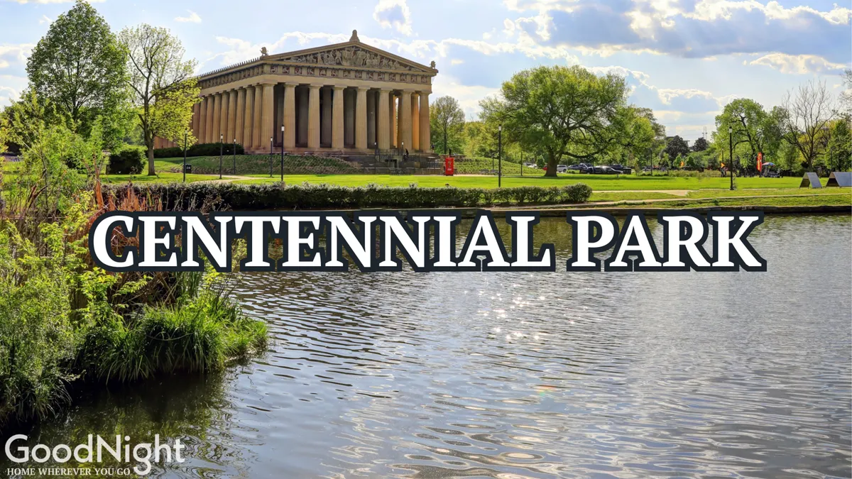 A scenic view of the Parthenon replica in Centennial Park, set beside a tranquil water surface and surrounded by lush greenery. People can be seen walking, picnicking, and enjoying the outdoors.