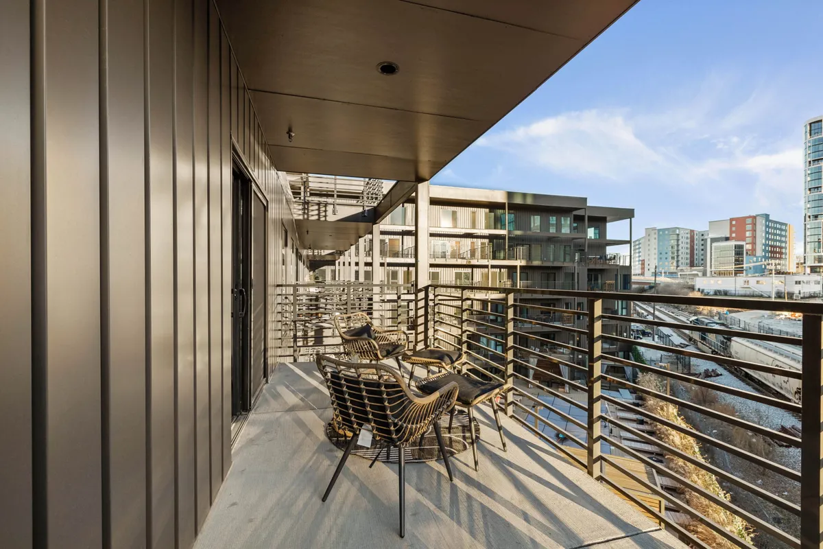 A modern balcony with urban views, featuring comfortable seating and a sleek railing. The setting suggests a calm atmosphere perfect for enjoying the fresh air, sharing conversations, or quietly admiring the cityscape at different times of day.