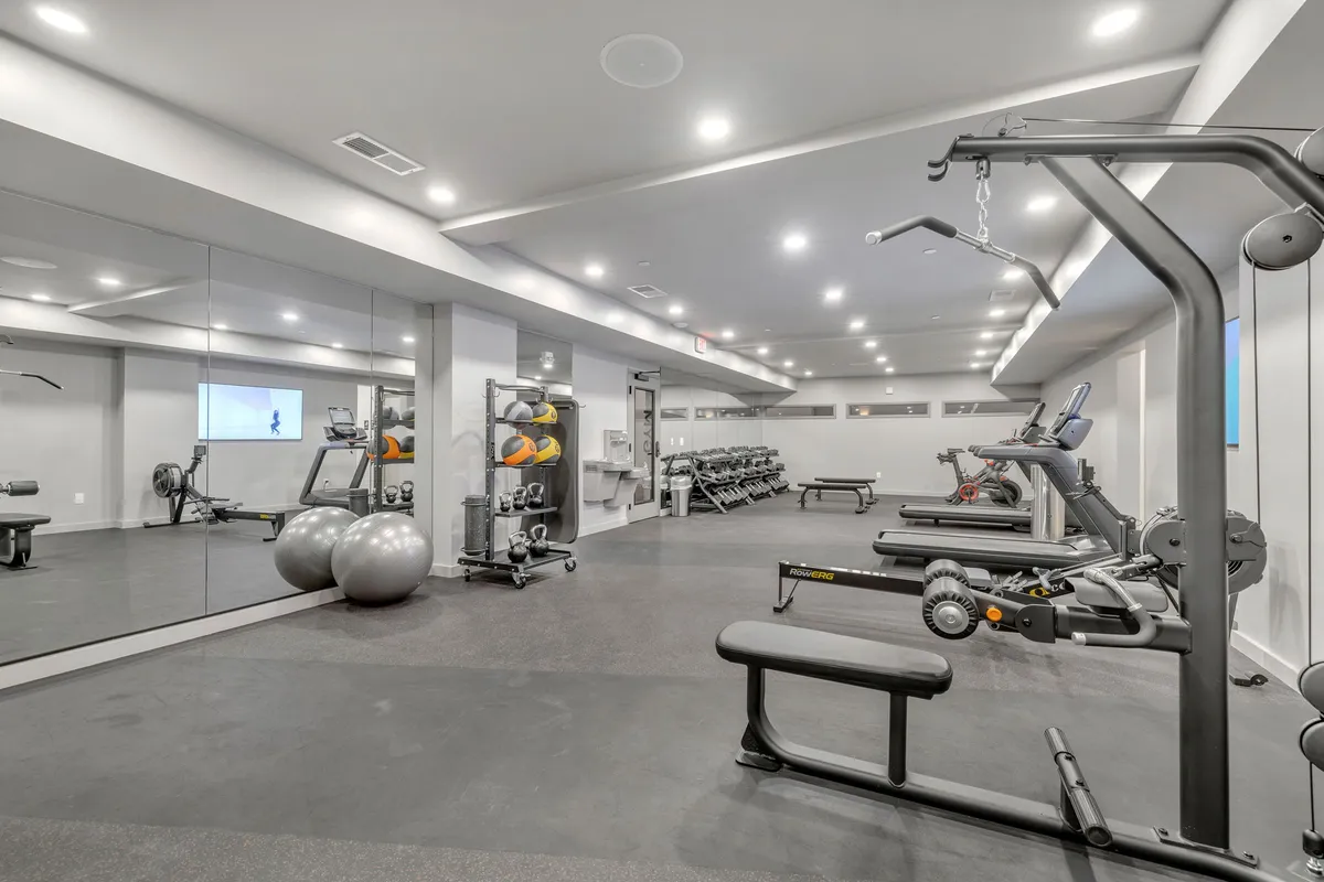 An interior shot of a fully equipped fitness center, featuring state-of-the-art exercise equipment, spacious mirrors, and a bright, energizing atmosphere. The gym is clearly designed for a variety of workouts, supporting both solo and group fitness routines.