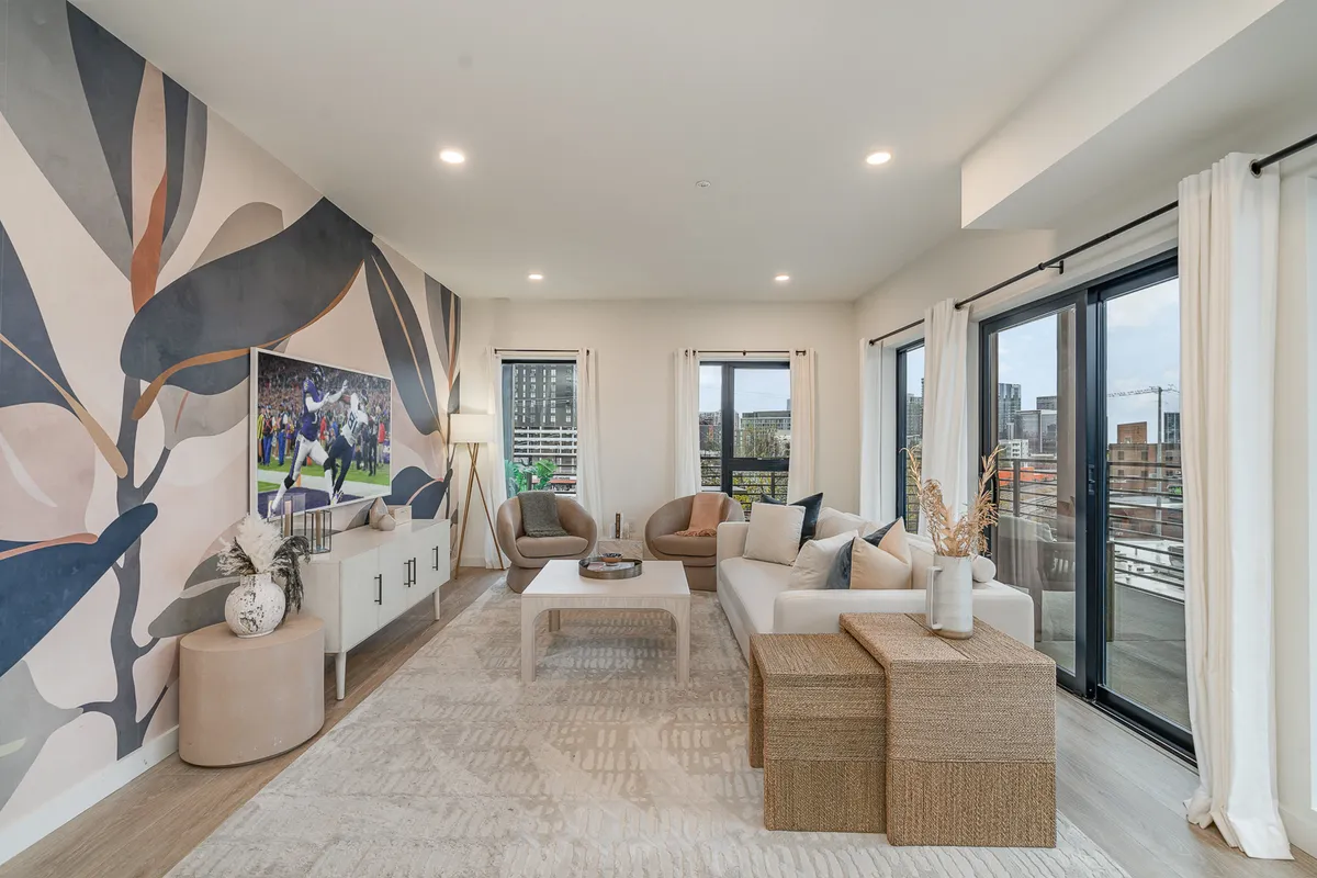 This inviting lounge area features stylish, comfortable seating, a large wall mural, a coffee table, and expansive windows revealing a cityscape view. The space is ideal for social gatherings, watching TV, or enjoying morning coffee with friends.
